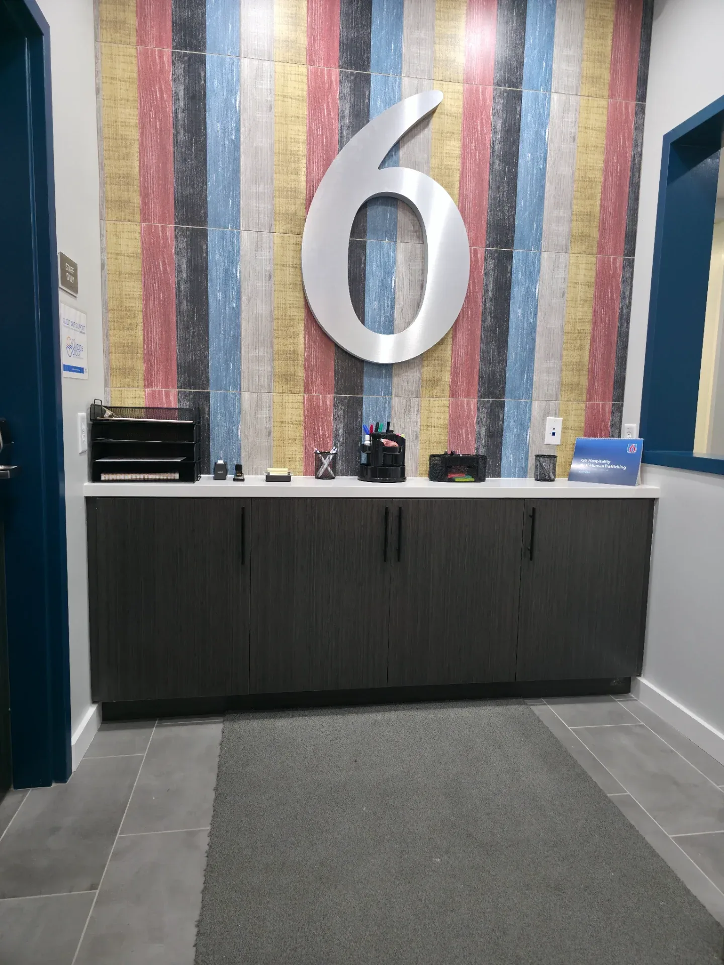Dark laminate reception credenza with four doors below a multicolor striped accent wall and large numeral signage